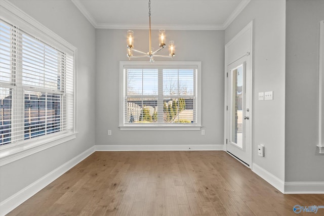 unfurnished dining area with a healthy amount of sunlight, an inviting chandelier, ornamental molding, and wood finished floors