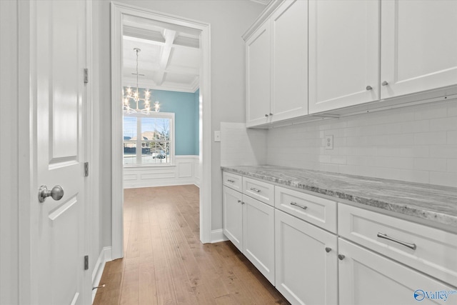 interior space featuring coffered ceiling, a wainscoted wall, wood finished floors, an inviting chandelier, and beam ceiling