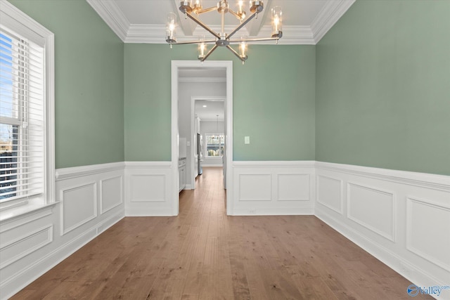 unfurnished dining area featuring an inviting chandelier, ornamental molding, a wealth of natural light, and wood finished floors