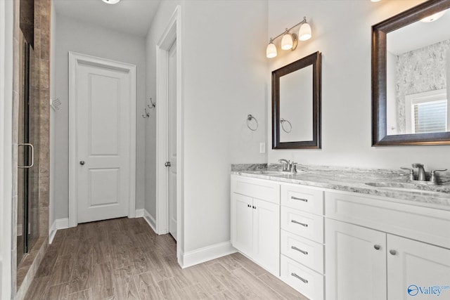 bathroom with a stall shower, double vanity, a sink, and wood finished floors