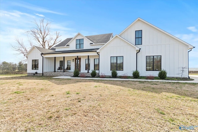 modern farmhouse style home featuring covered porch, board and batten siding, a shingled roof, and a front lawn