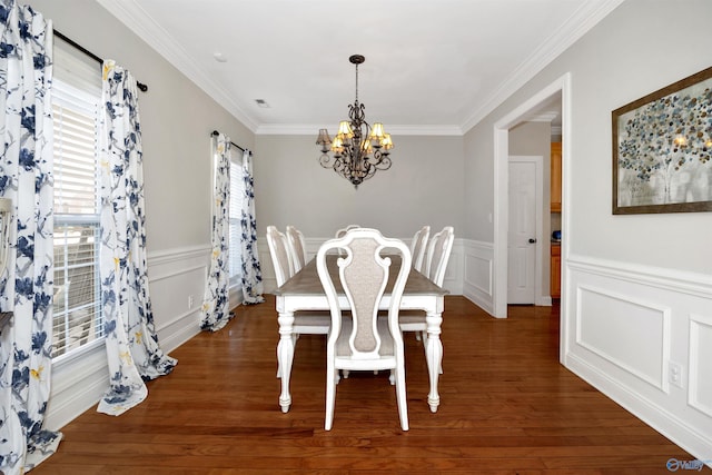 dining room featuring wood finished floors, wainscoting, a decorative wall, ornamental molding, and an inviting chandelier