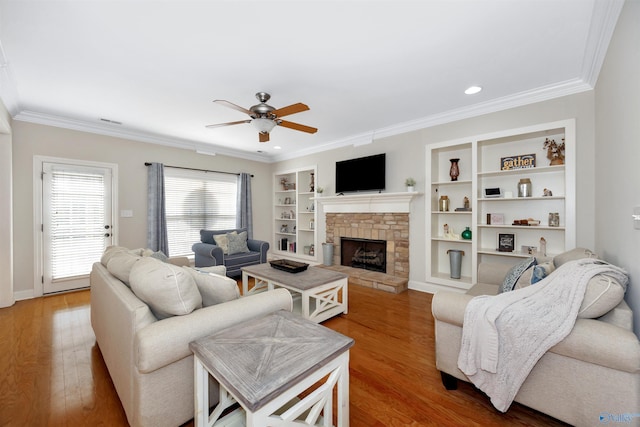 living area featuring crown molding, ceiling fan, wood finished floors, a stone fireplace, and built in features