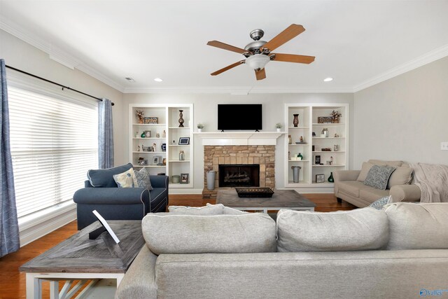 living area featuring built in features, ceiling fan, wood finished floors, and a stone fireplace