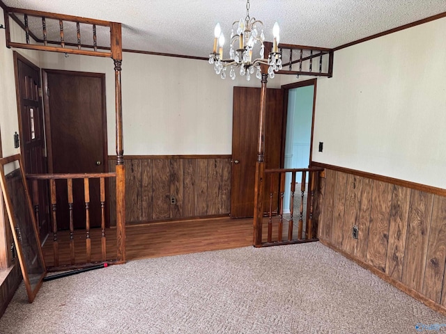 carpeted spare room with an inviting chandelier, a wainscoted wall, wooden walls, and a textured ceiling