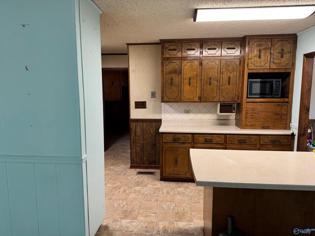 kitchen with light countertops, a textured ceiling, backsplash, a wainscoted wall, and visible vents