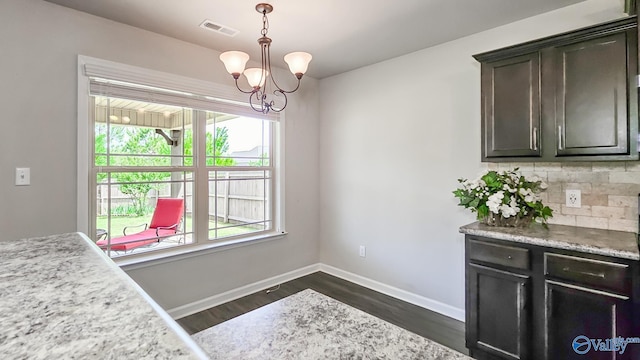 unfurnished dining area with baseboards, dark wood-style flooring, a notable chandelier, and visible vents