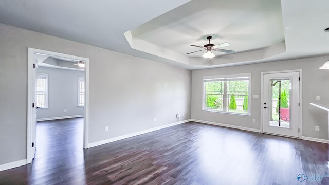 unfurnished living room featuring plenty of natural light, a ceiling fan, dark wood-type flooring, and a tray ceiling
