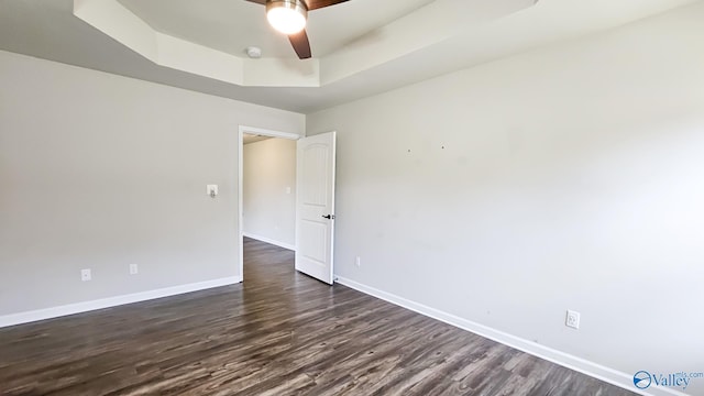 spare room featuring a tray ceiling, baseboards, a ceiling fan, and dark wood-type flooring