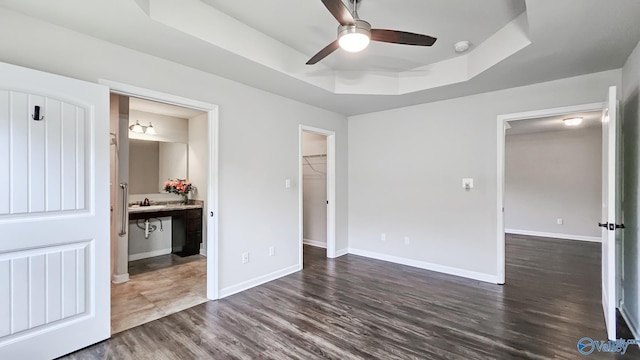 unfurnished bedroom featuring dark wood-style flooring, baseboards, a spacious closet, ensuite bathroom, and a tray ceiling