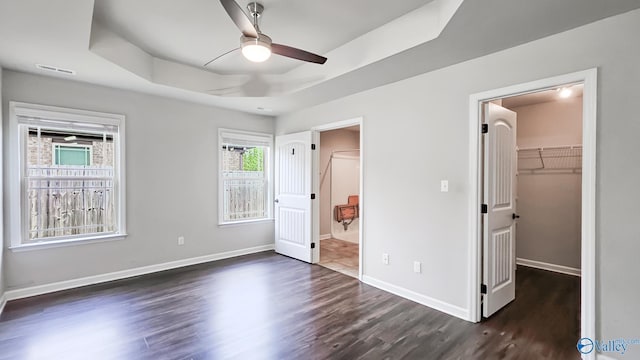 unfurnished bedroom featuring a walk in closet, a tray ceiling, dark wood finished floors, and visible vents