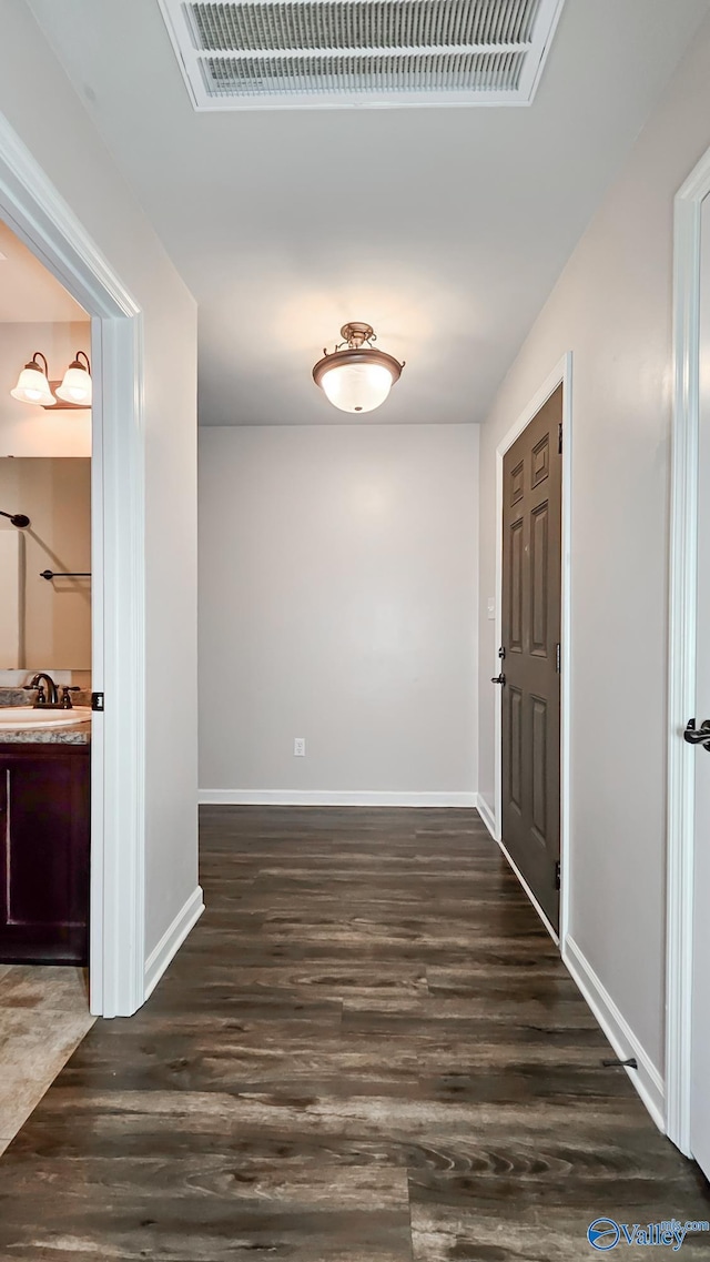 hall featuring baseboards, dark wood-style floors, and a sink