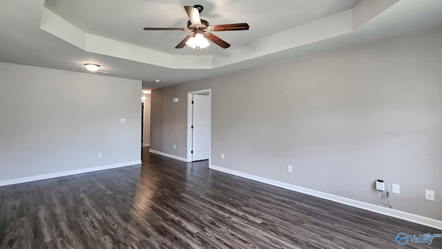 unfurnished room with baseboards, ceiling fan, a tray ceiling, and dark wood-style flooring