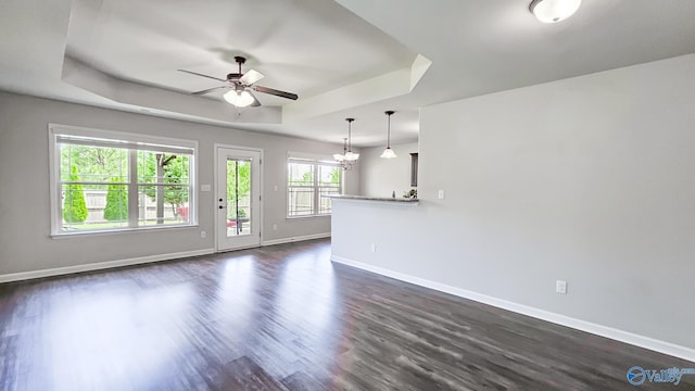 unfurnished living room featuring a raised ceiling, baseboards, dark wood-style floors, and ceiling fan with notable chandelier
