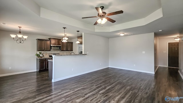 unfurnished living room featuring a raised ceiling, ceiling fan with notable chandelier, and dark wood-style floors