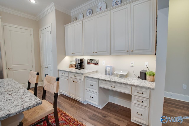 kitchen with built in desk, white cabinetry, dark hardwood / wood-style flooring, crown molding, and light stone countertops