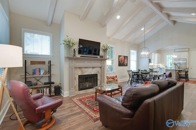 living room featuring beam ceiling, high vaulted ceiling, a notable chandelier, a fireplace, and light hardwood / wood-style floors