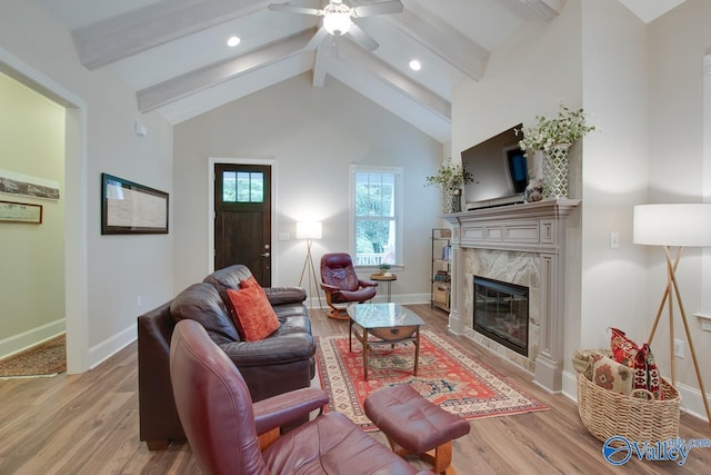 living room with beam ceiling, high vaulted ceiling, ceiling fan, a premium fireplace, and light hardwood / wood-style floors