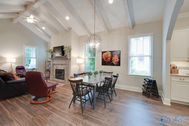 dining space with dark wood-type flooring, a premium fireplace, high vaulted ceiling, ceiling fan with notable chandelier, and beamed ceiling