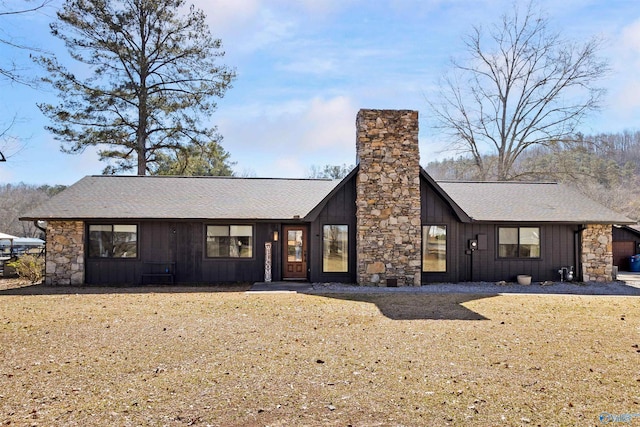 view of front of property with stone siding, roof with shingles, board and batten siding, a chimney, and a front yard