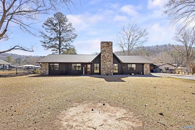 view of front of house featuring a mountain view, stone siding, board and batten siding, a front lawn, and a chimney