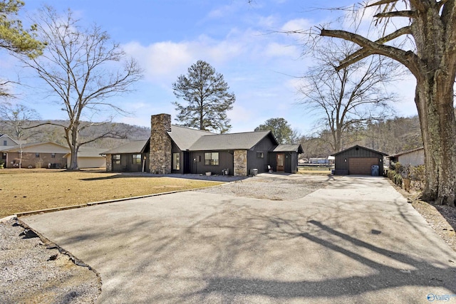 view of front of house featuring aphalt driveway, a front yard, a chimney, and an outbuilding