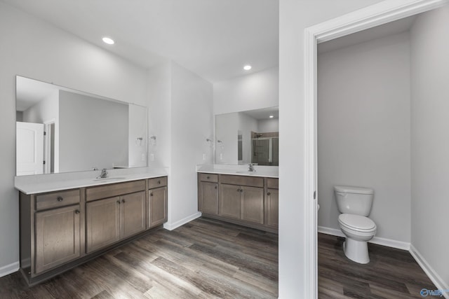 bathroom featuring a shower stall, two vanities, wood finished floors, and a sink