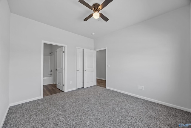 unfurnished bedroom featuring dark carpet, connected bathroom, baseboards, and a ceiling fan