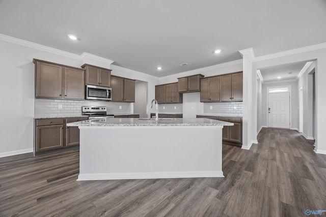 kitchen featuring light stone counters, dark wood-style floors, a kitchen island with sink, a sink, and stainless steel appliances