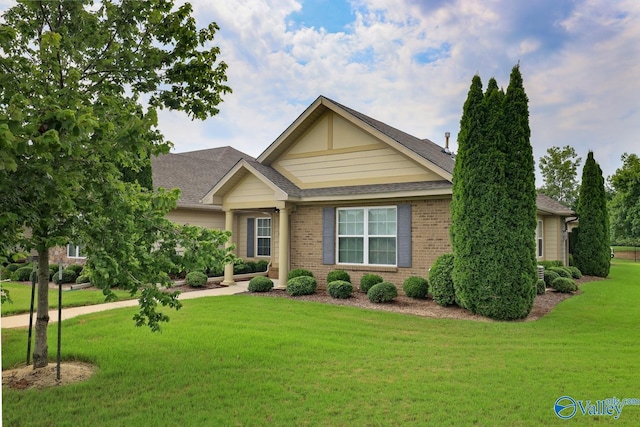 view of front facade featuring a shingled roof, a front yard, and brick siding