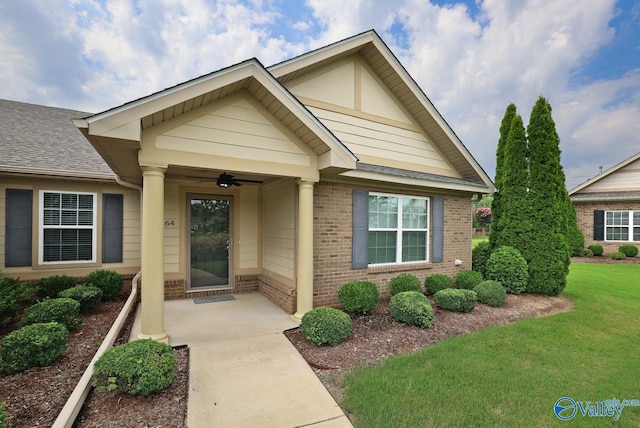 property entrance with a yard, brick siding, a shingled roof, and a ceiling fan