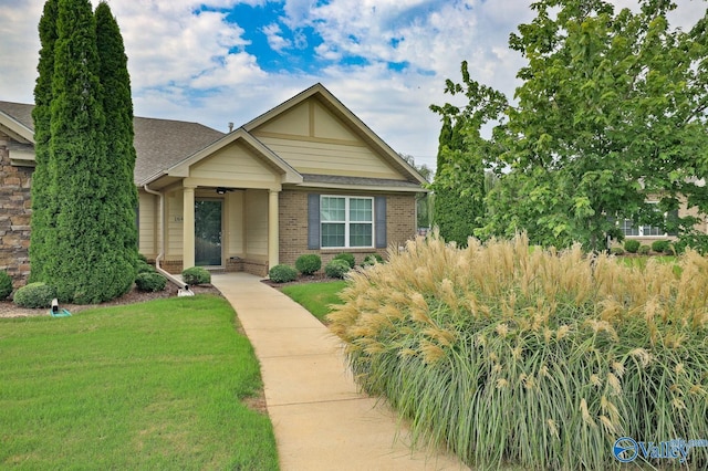 view of front of house with a shingled roof, a front yard, and brick siding