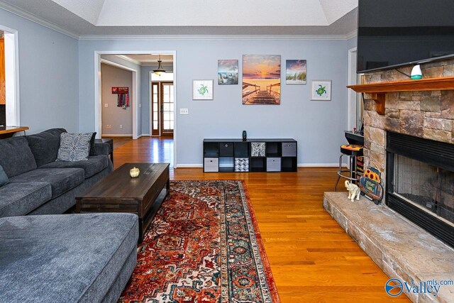 living room featuring baseboards, ornamental molding, wood finished floors, and a stone fireplace