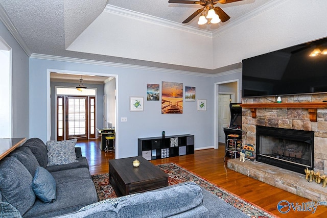 living room with ceiling fan, ornamental molding, wood finished floors, a textured ceiling, and a stone fireplace