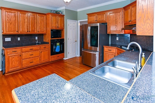 kitchen featuring ornamental molding, a sink, wood finished floors, under cabinet range hood, and black appliances