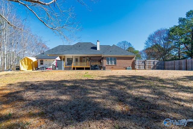 rear view of house featuring a chimney, fence, a lawn, and brick siding