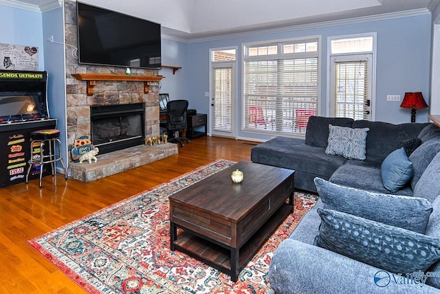 living area with ornamental molding, a stone fireplace, and wood finished floors