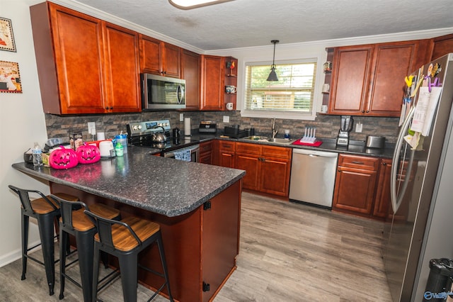 kitchen with sink, kitchen peninsula, decorative light fixtures, appliances with stainless steel finishes, and light hardwood / wood-style floors