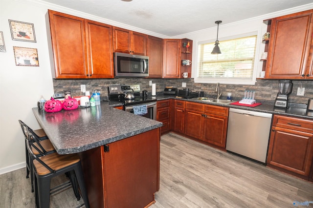 kitchen with light wood-type flooring, tasteful backsplash, kitchen peninsula, stainless steel appliances, and decorative light fixtures