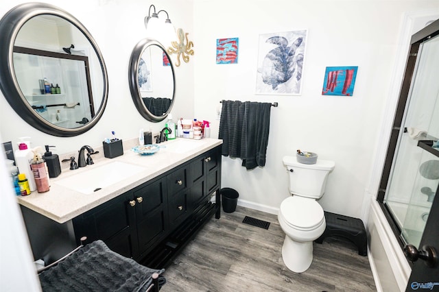 full bathroom featuring bath / shower combo with glass door, hardwood / wood-style flooring, vanity, and toilet