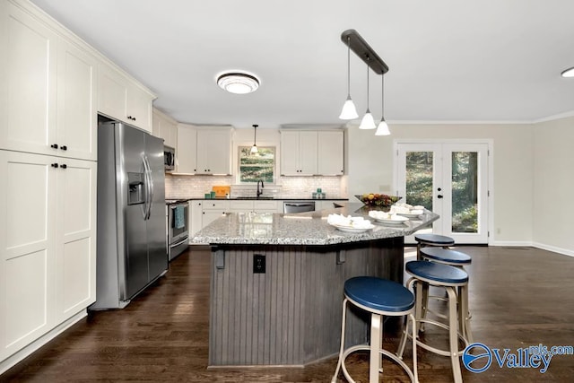 kitchen with white cabinetry, light stone counters, decorative light fixtures, a center island, and stainless steel appliances