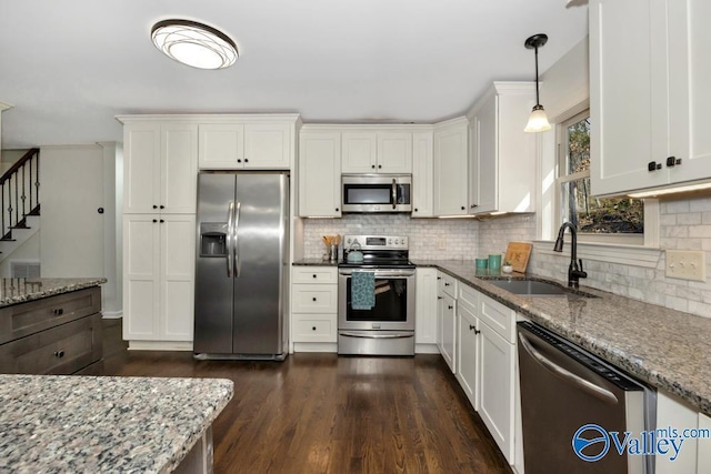 kitchen with sink, white cabinetry, appliances with stainless steel finishes, pendant lighting, and light stone countertops