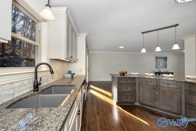 kitchen with white cabinetry, stone countertops, sink, and hanging light fixtures