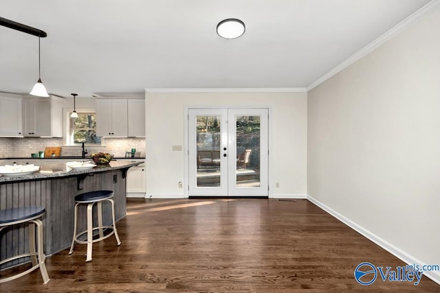 kitchen featuring dark stone countertops, hanging light fixtures, white cabinets, a kitchen bar, and decorative backsplash