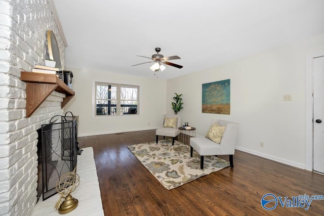 sitting room with a brick fireplace, dark hardwood / wood-style floors, and ceiling fan