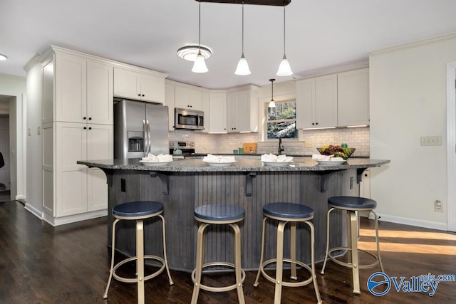 kitchen featuring a breakfast bar, stainless steel appliances, white cabinets, dark hardwood / wood-style flooring, and dark stone counters