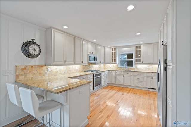 kitchen featuring appliances with stainless steel finishes, white cabinets, decorative backsplash, light stone counters, and kitchen peninsula