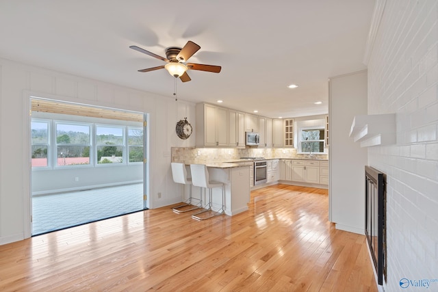 kitchen with a breakfast bar, appliances with stainless steel finishes, white cabinetry, light hardwood / wood-style floors, and kitchen peninsula