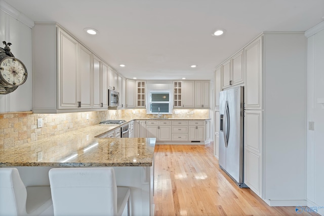 kitchen with sink, white cabinets, kitchen peninsula, stainless steel appliances, and light stone countertops