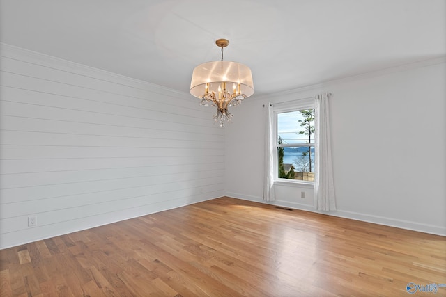 spare room featuring crown molding, light hardwood / wood-style flooring, and a chandelier